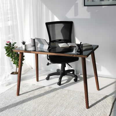 Scrivania moderna per casa e ufficio con ripiano in vetro temperato fumé e legno massello, gambe in legno di faggio color noce opaco dai toni caldi. Dimensioni cm 110x60x73h