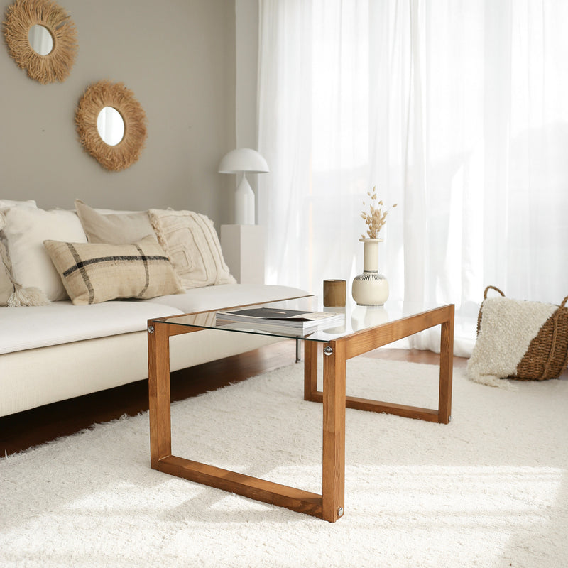 Tavolino basso da salotto in stile moderno con gambe in legno massello di pino e ripiano in vetro trasparente temperato. Disponibile nella colorazione noce opaco e rovere chiaro opaco. Dimensioni cm 85x55x40h
